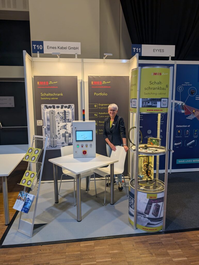 Messestand mit Schaltschränken und Produktportfolio, betreut von einer Frau im Business-Outfit.