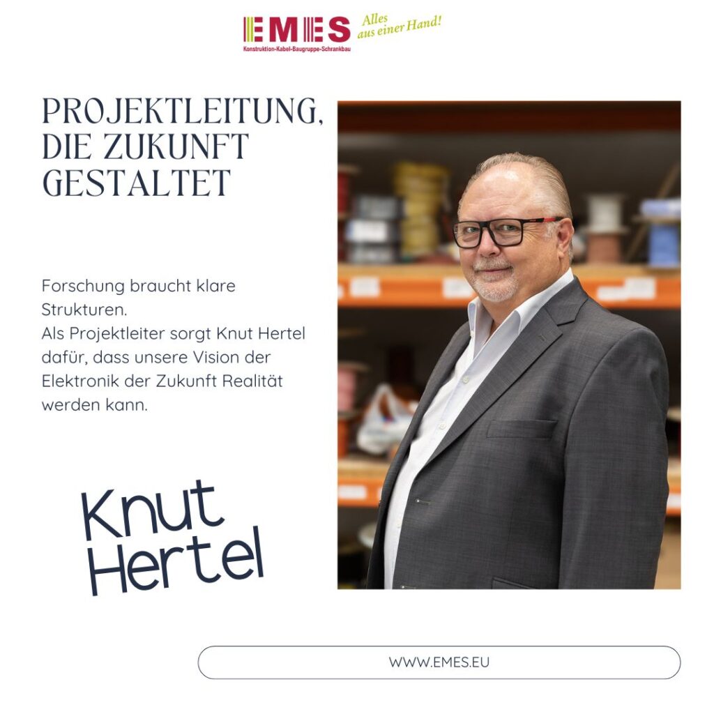 Projektleiter in Anzug steht in einer Produktionsumgebung vor Regalen mit Kabelspulen.